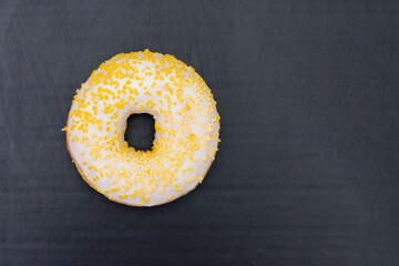 Donut with white sugar glazed and sprinkled with yellow pastry crumbs, on a black background with copy space
