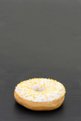 Donut with white sugar glazed and sprinkled with yellow pastry crumbs, on a black background with copy space