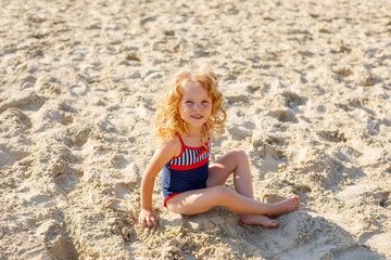 little girl sitting on the beach on the sand summer;