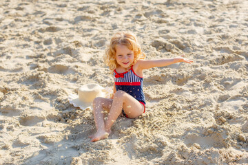 little girl sitting on the beach on the sand summer;