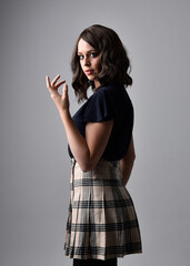 Close up portrait of pretty brunette woman wearing tartan skirt and blouse.  Posing with gestured hands against a  studio background.