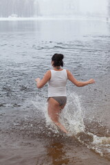 Swimming in the winter. Woman enters ice bathing water