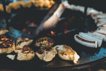 Fleisch und halbe Bratwürstchen auf einem Rundgrill oder Feuerschale