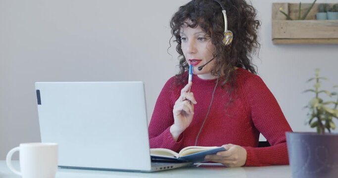 
Woman working as a telemarketer with headphones in an office or from home writing in a notebook. Female receiving online classes