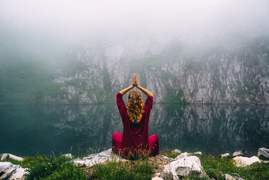Meditating woman on white rock near body of water