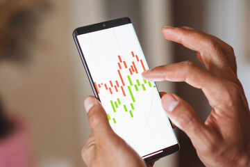 Closeup of a broker using a mobile phone with a graph on a touchscreen. Businessman working with statistics, looking at a phone screen with a diagram with finance trade.