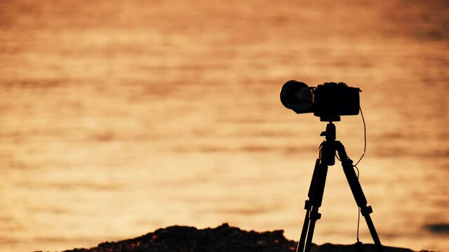 Camera on tripod taking travel picture from seaside landscape, sunset colors.