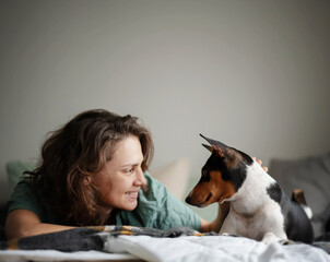 Beautiful happy young woman with african terrier bassenji dog on bed looking at each other, close-up portrait