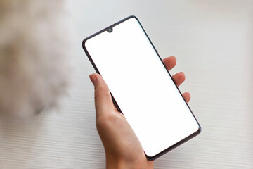 Closeup mockup image of a woman's hand holding mobile phone with blank white screen in a cozy space.