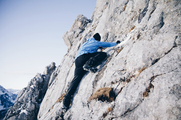 Sportlicher Alpinist klettert schneebedecktes Gestein und winterliches Gebirge entlang