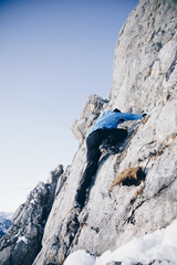 Sportlicher Alpinist klettert schneebedecktes Gestein und winterliches Gebirge entlang