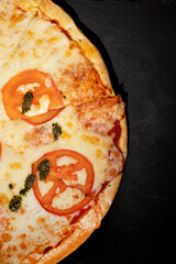 Half fresh pizza margarita with pesto sauce on black stone plate. Vertical, top view