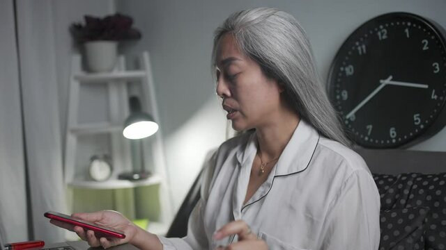 Portrait of stressed woman reading taxt in smart phone while smoking in the bed and thinking the solution while working in front of a computer.
