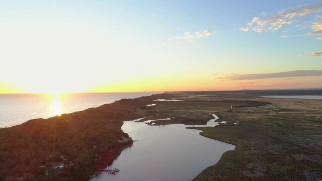 Backward flight over ocean coastline at sunset in Marlo, Australia