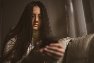 Teen girl excessively sitting at the phone at home. Sad depressed young teenager holding mobile smart phone.