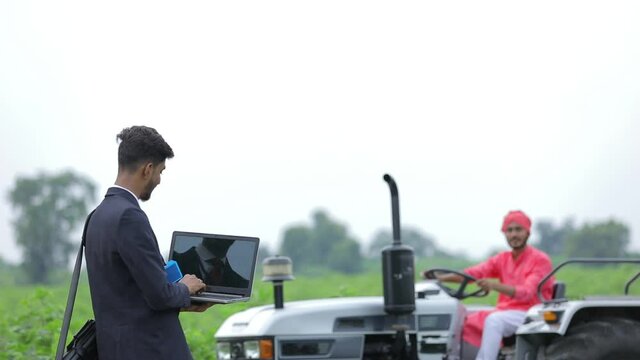 Young indian agronomist or banker showing laptop screen with farmer at agriculture field