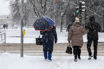 In snowstorm people cross the street. Winter, frost and urban environment