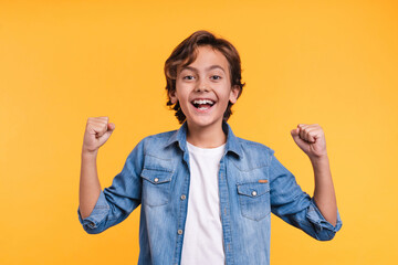 Excited young boy is happy like a winner in casual clothes isolated over yellow background