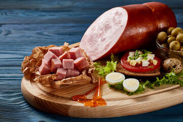 Mortadella with vegetables and herbs on a wooden plate on a wooden table.