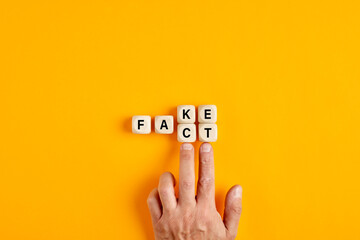 Male hand pushing the wooden cubes and transforming the word fake to fact - obrazy, fototapety, plakaty