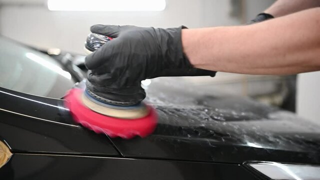 Car detailing - hands with orbital polisher in auto repair shop in slow motion.