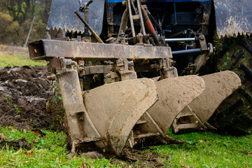 Fototapeta premium Land cultivation,tractor plows the ground, a blue small tractor and a plow with three knives.