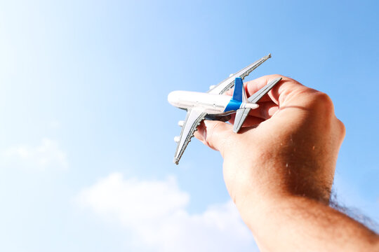 close up photo of man's hand holding toy airplane against blue sky with clouds