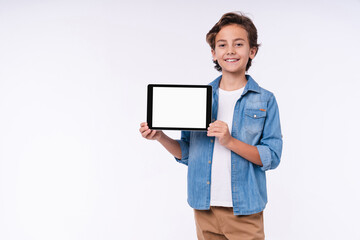 Smiling little boy in casual clothes presenting blank screen of the tablet isolated over white...