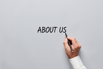 Male hand writing the word about us on gray background. Promoting the company or business publicity