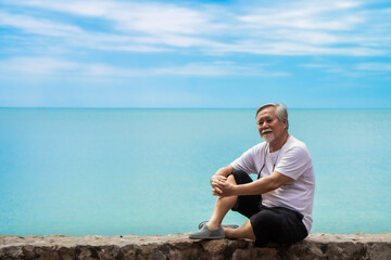 old gray-haired Asian man wearing casual clothes, enjoying the view of the sea and sky background.