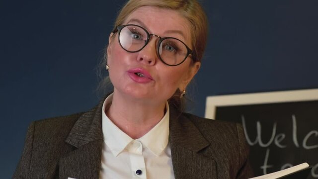 Senior teacher is explaining something from a book during a lesson near the blackboard
