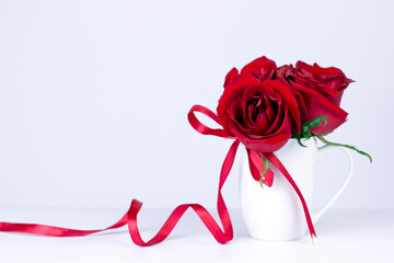 Red roses bouquet with red ribbon in white cup on wooden background. Valentine day gift card with copy space.