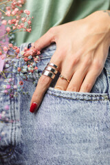 Close shot of  woman hand fingers wearing two rings, bouquet  of colorful dried flowers, hold hand in pocket of blue denim pants jeans, light green shirt