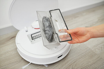 Woman opens lid of robot vacuum cleaner to show transparent plastic container with small rubbish on...