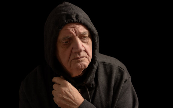 portrait vieil homme triste avec capuche relev&eacute;e et regard abaiss&eacute; sur fond noir 