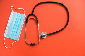 Cardiologist doctor tool.Medical mask, stethoscope top view on bright orange background. Selective...