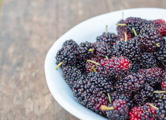 Ripe mulberries on white a dish on wooden table. Tasty berry with copy space for text. Top view....