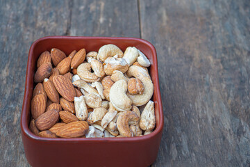 Almonds and cashew nuts in a brown bowl on a wooden table. Top view. Space for text. Concept of healthy fruit and snack