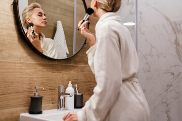 Beautiful young woman in bathrobe applying makeup