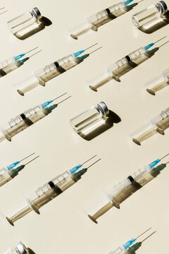 Syringes and COVID-19 vaccine vials on yellow background
