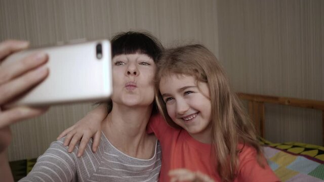 Video Call Family Selfie. Portrait Mother and Kids Kissing on Camera. Happy Mother With Her Kids are Making Selfie or Video Call to Father or Relatives in Bed. Technology, New Generation Parenthood.