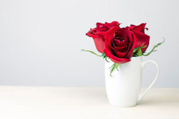 Red roses bouquet in white cup on wooden background. Valentine day gift card with copy space.