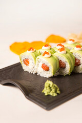 Close up to Japanese sushi roll with avocado and red caviar on top served with wasabi on black plate on white marble background. Raw Salmon, cream cheese wrapped in rice and nori seaweed. Inside out
