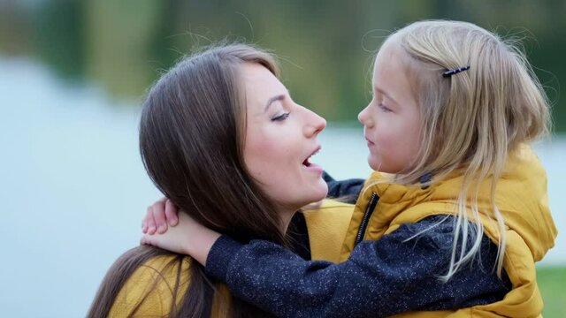 Daughter kissing mother on nature. Beautiful young woman and her charming little daughter are hugging and smiling. Daughter hugging mother on nature.