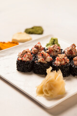 Close up of Japanese black rice sushi roll with unagi eel served with ginger, wasabi on square plate. Heart shapes of basil, garlic, turmeric powder spices on white marble background
