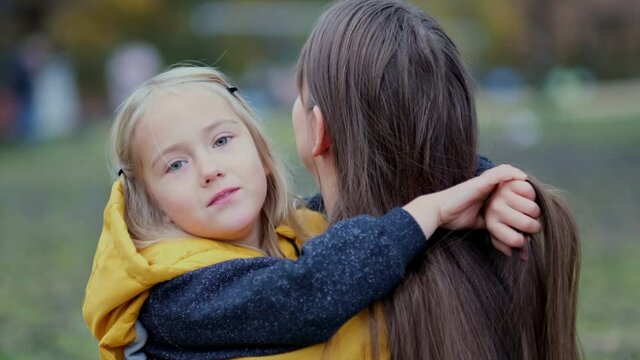 Daughter hugging mother on nature. Beautiful young woman and her charming little daughter are hugging and smiling. Daughter hugging mother on nature.