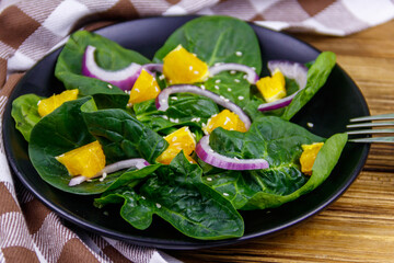 Tasty salad with spinach, orange, red onion and sesame seeds on wooden table. Healthy food or vegetarian concept