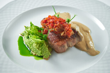 Appetizing pork steak with tomato salsa, mushroom sauce and mashed peas in a white plate. Close up, selective focus