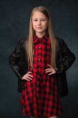 girl child in a plaid dress and leather jacket on a gray fabric background