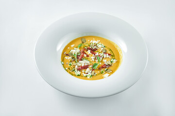 Appetizing pumpkin cream soup with feta, sun-dried tomatoes and microgreen on a white background in a white plate